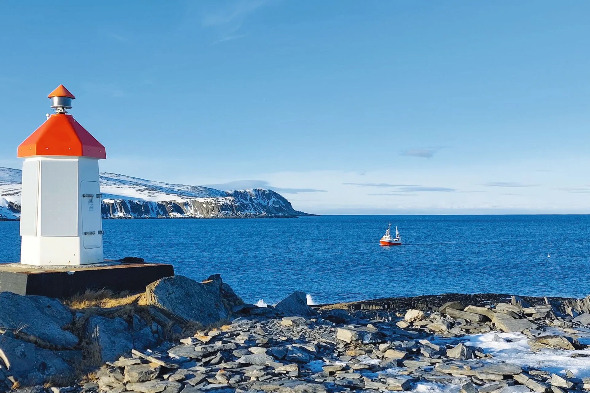 Et hvitt fyr med rødt tak på en steinete kyst.