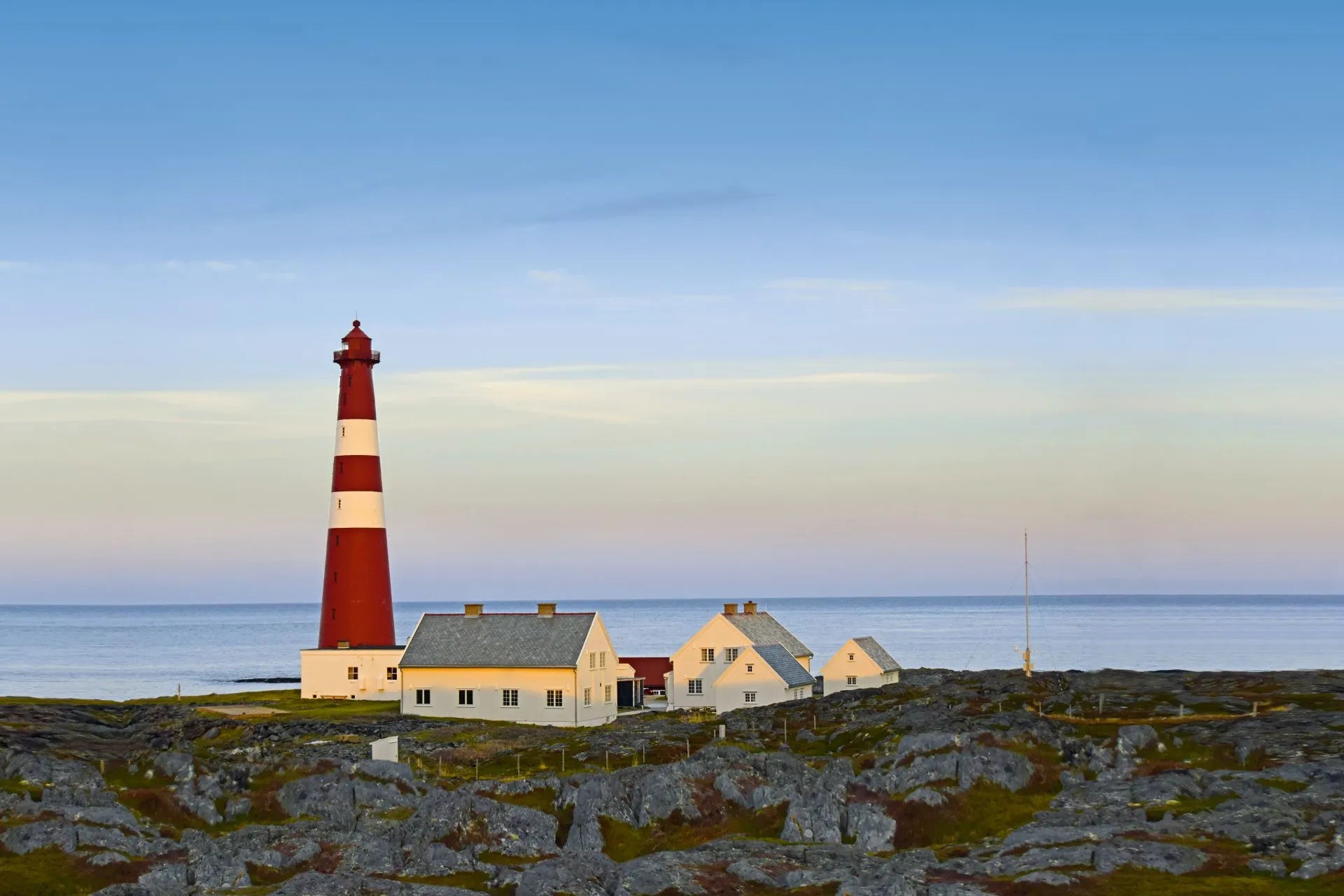 Et rødt og hvitt fyr på en steinete strand ved sjøen.