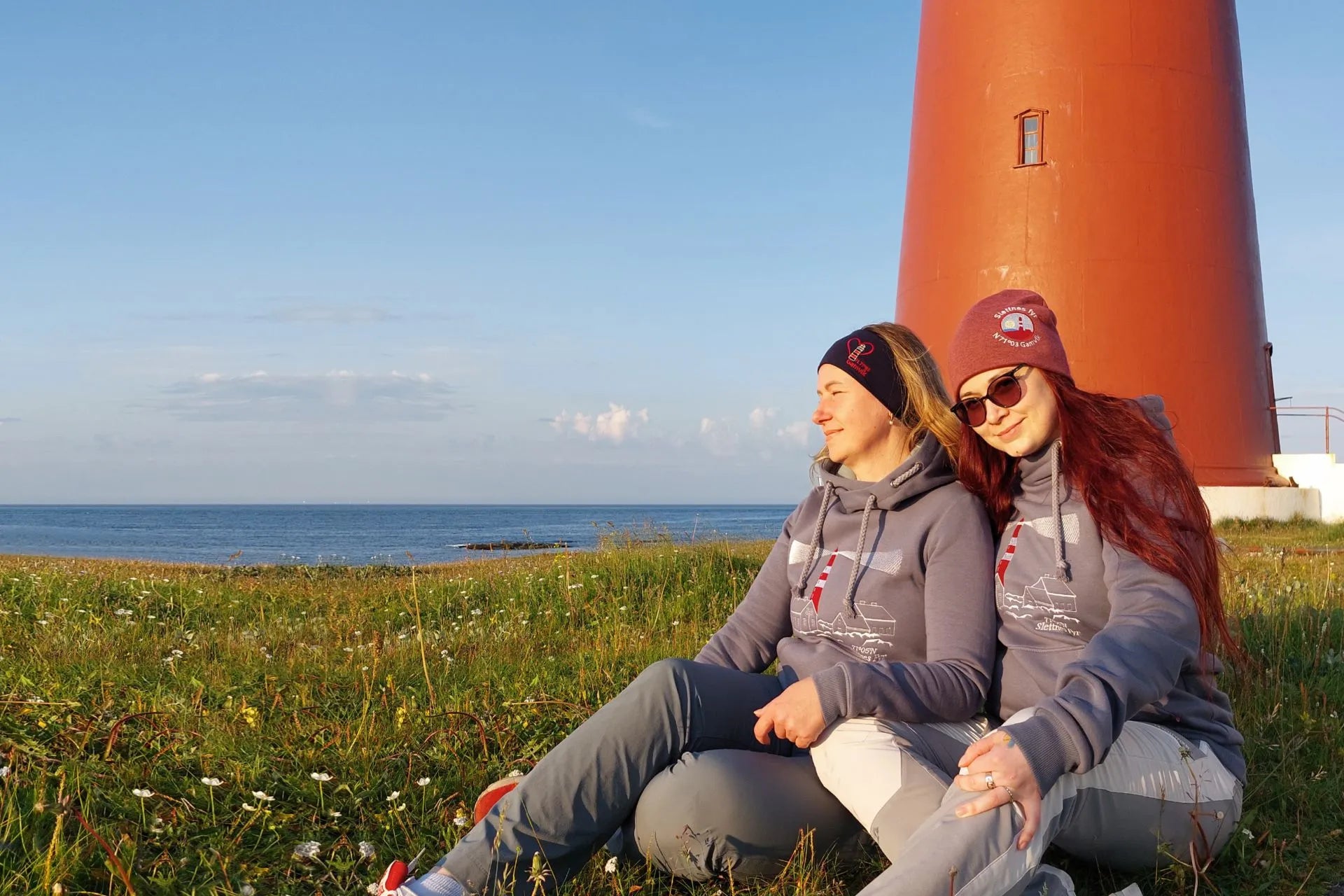 Kvinner smiler ved foten av et oransje fyr på gresset.