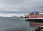 Mehamn havn i Finnmark med røde sjøhus på kaia, snødekte fjell og stille vinterlig sjø