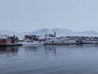 Mehamn havn i Finnmark med kirken og bebyggelse, snø og lavt vinterlys over rolig vann