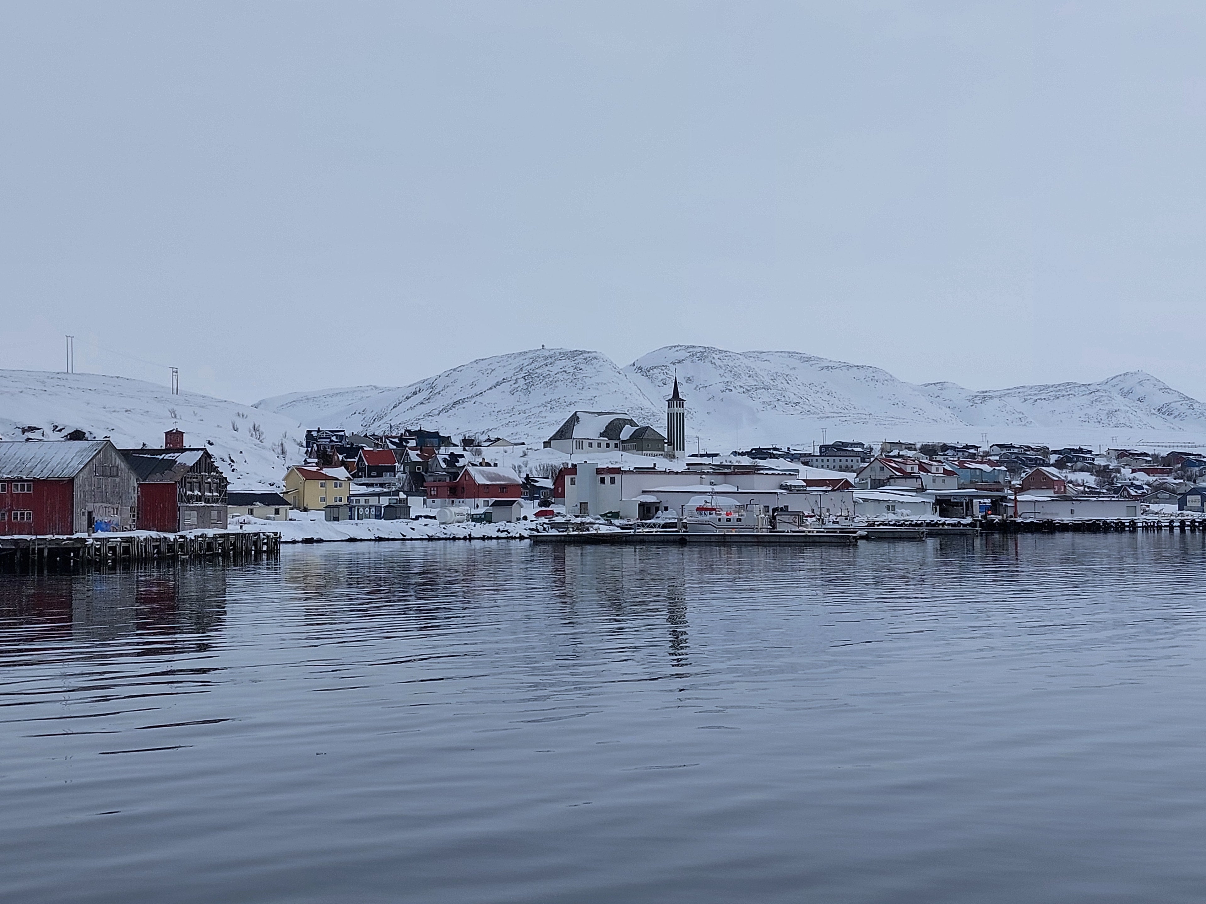 Mehamn havn i Finnmark med kirken og bebyggelse, snø og lavt vinterlys over rolig vann