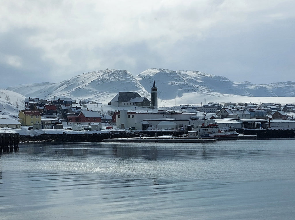 Mehamn havn i Finnmark med kirken, snødekte fjell og stille sjø i rolig vinterlys