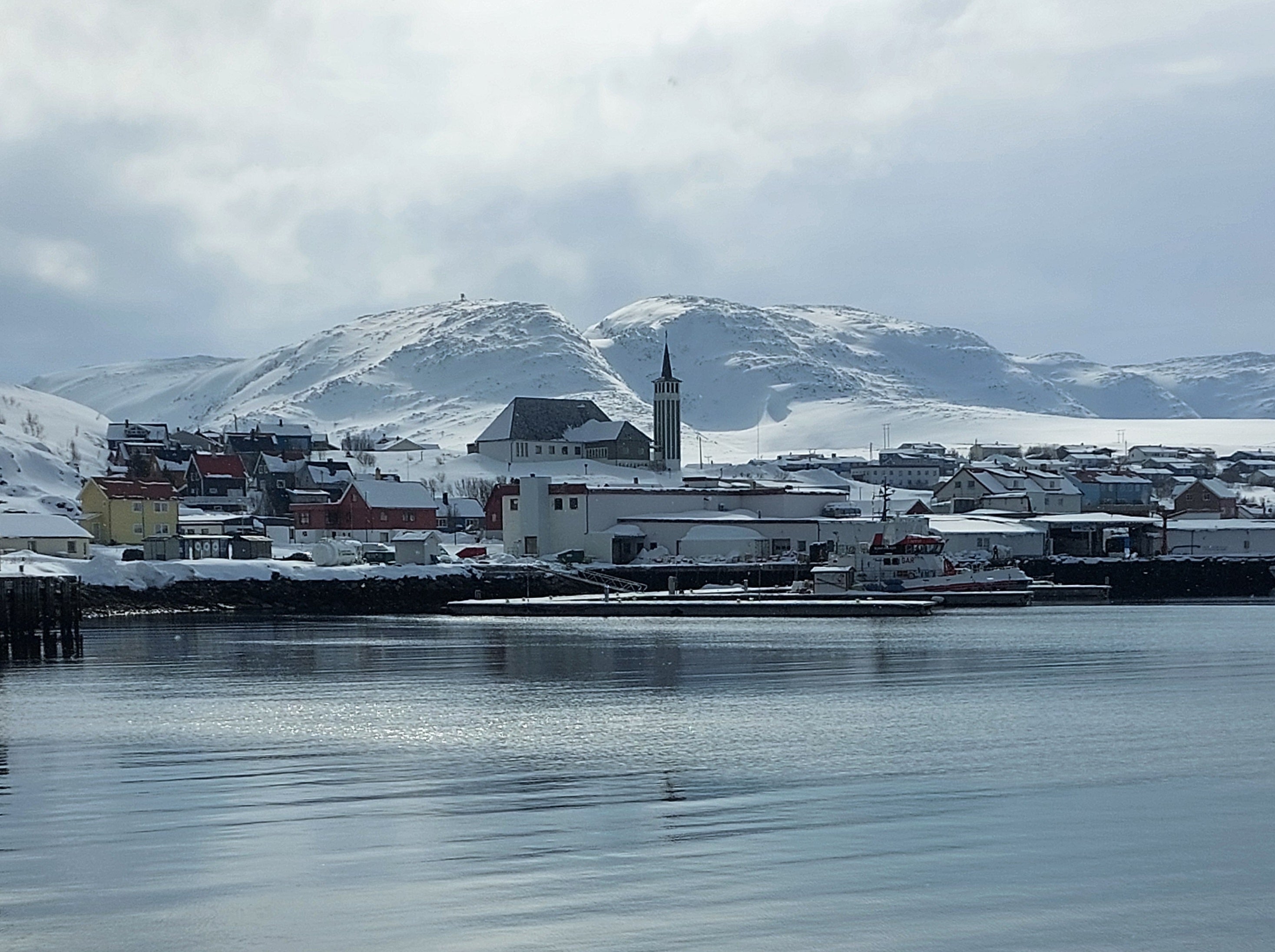 Mehamn havn i Finnmark med kirken, snødekte fjell og stille sjø i rolig vinterlys