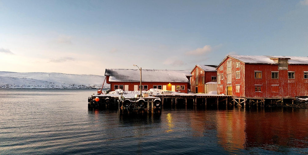 Kaia i Mehamn i Finnmark med røde sjøhus og stille vann i mykt kveldlys